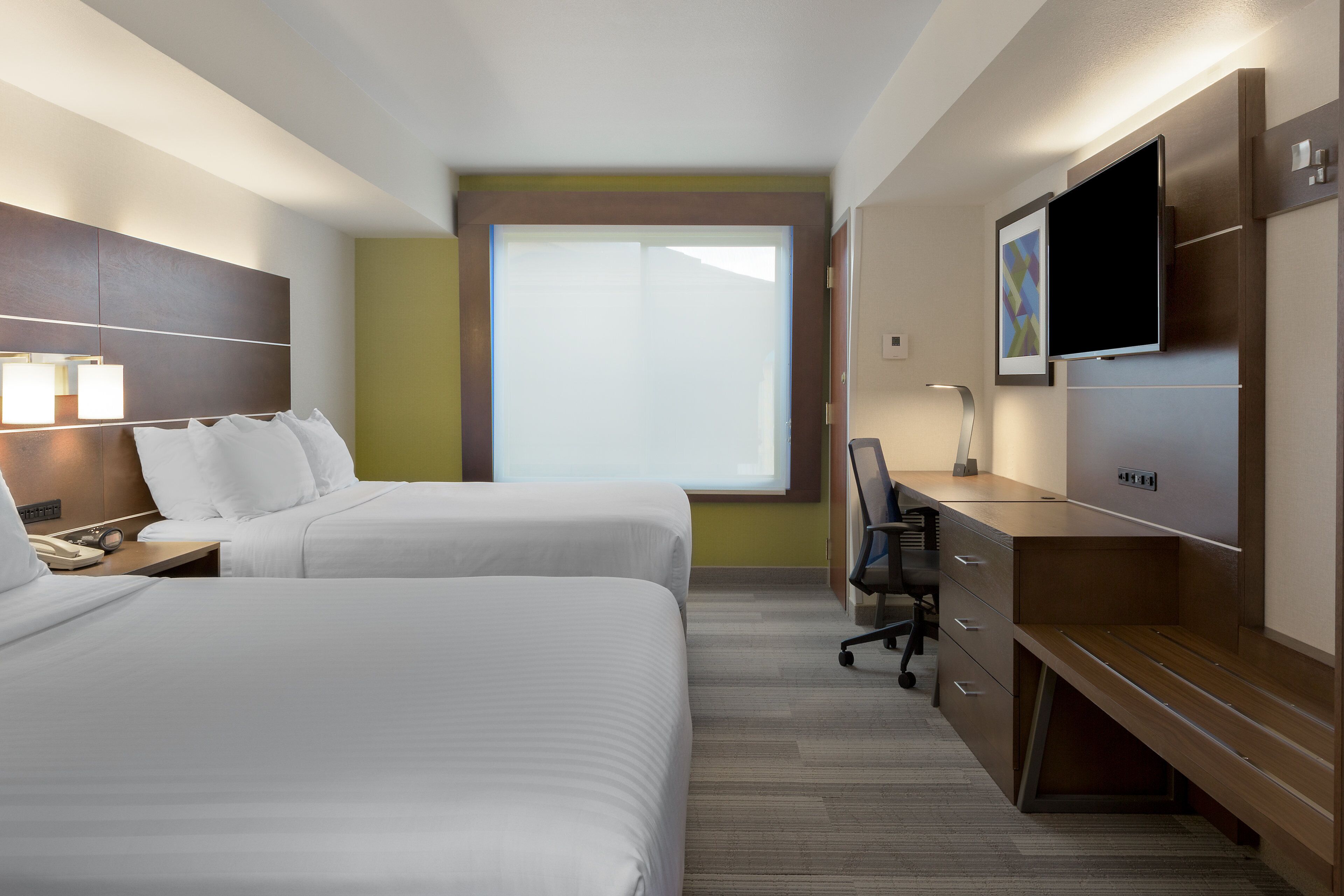 A hotel room with two beds, a desk, a TV, and a window.