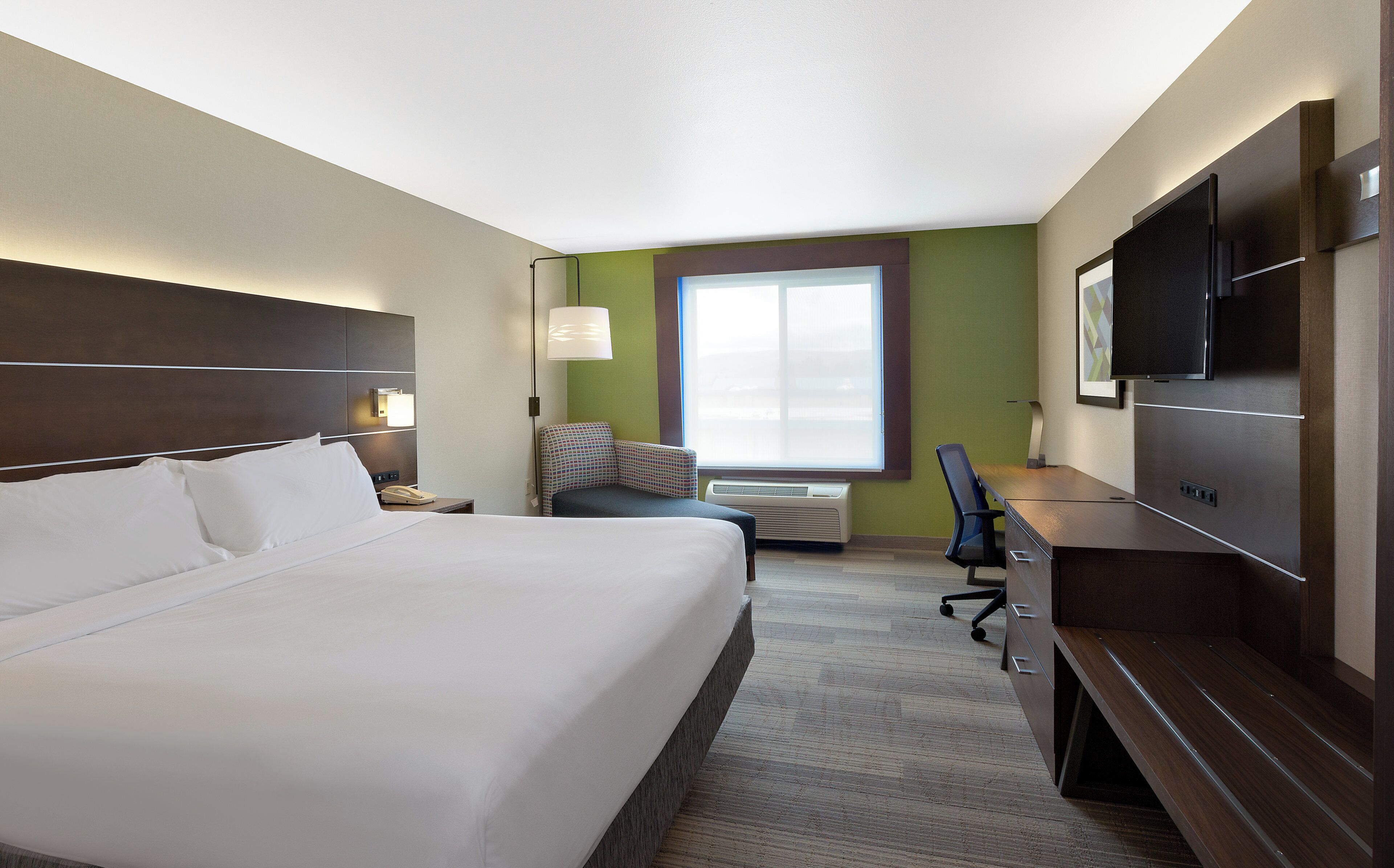 A hotel room with a bed, a desk, a chair, a television, and a window.