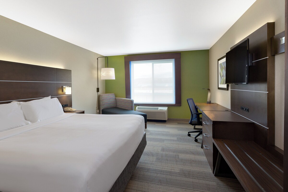 A hotel room with a large bed, a desk, a chair, a television, and a window.