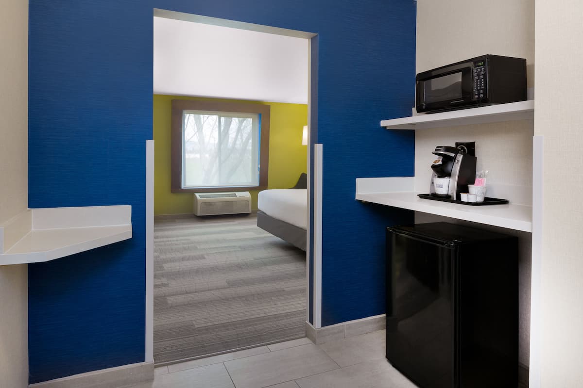 A modern hotel room with a bed, a microwave, a coffee maker, and a small refrigerator.