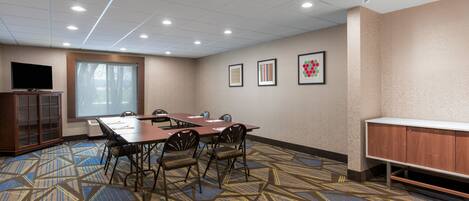 A conference room with a large table, chairs, a television, and framed pictures on the wall.