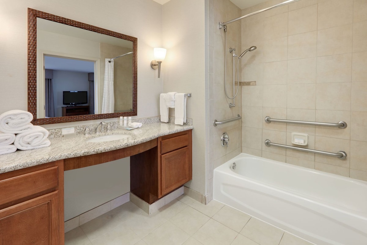 Une salle de bain moderne équipée d’un lavabo, d’un miroir, d’un porte-serviettes, d’une douche et de barres d’appui.