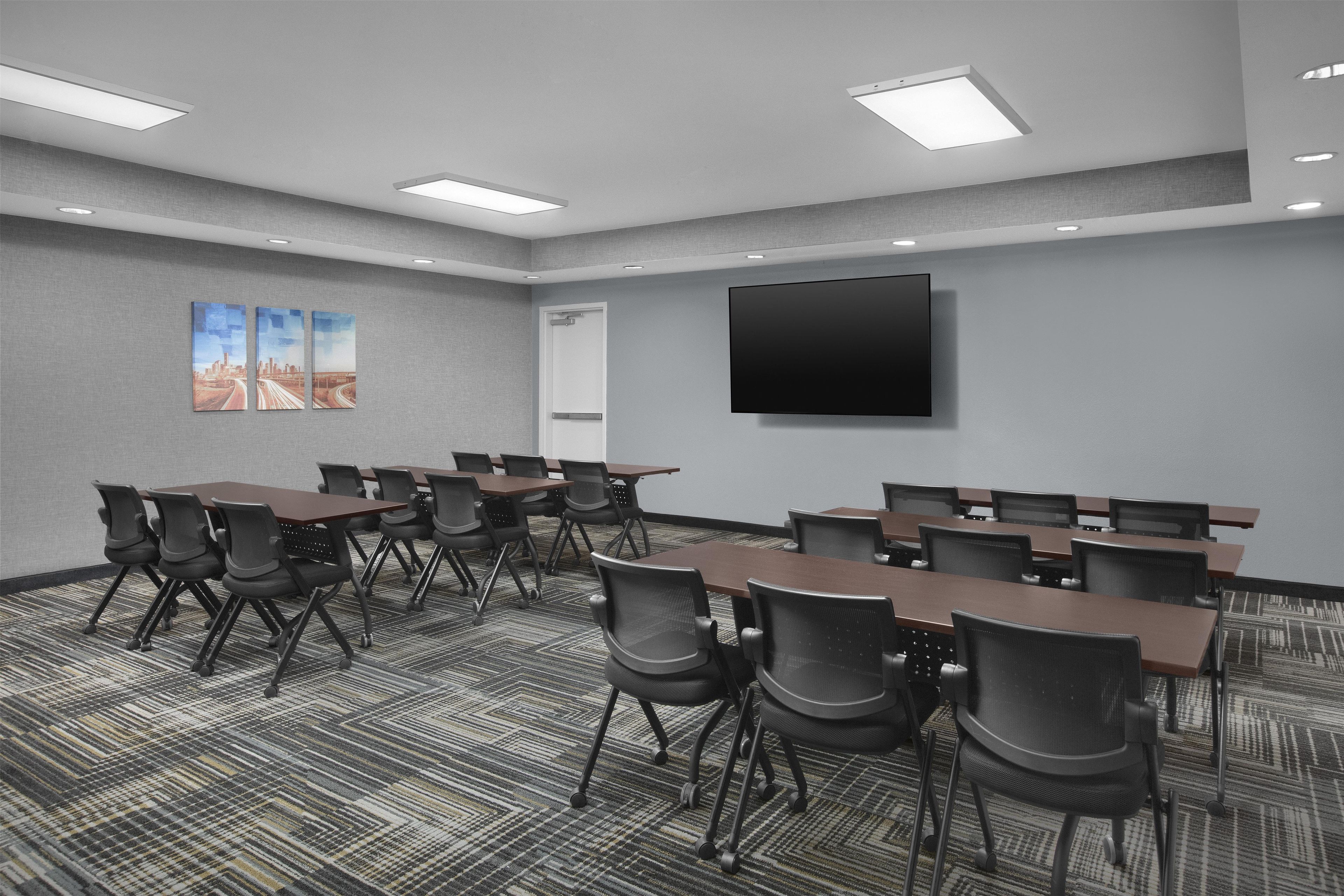 A conference room with a large flat-screen TV, multiple tables, and chairs.