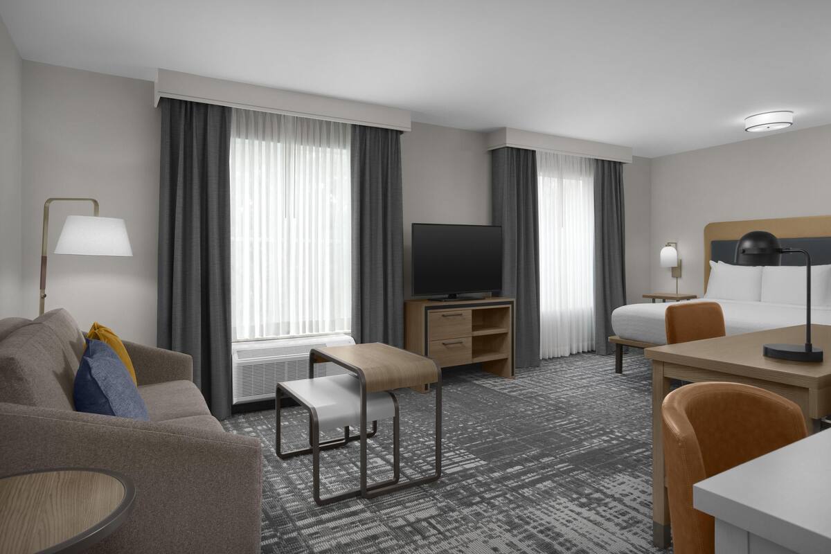 Ein Hotelzimmer mit einem Bett, einem Schreibtisch, einem Fernseher, einer Couch und einem Sessel.
