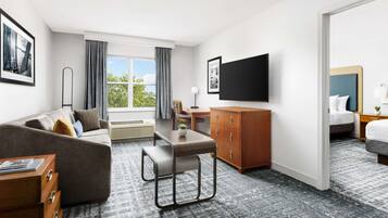 Quarto de hotel com sofá, mesa pequena, televisão, guarda-roupa e cama.