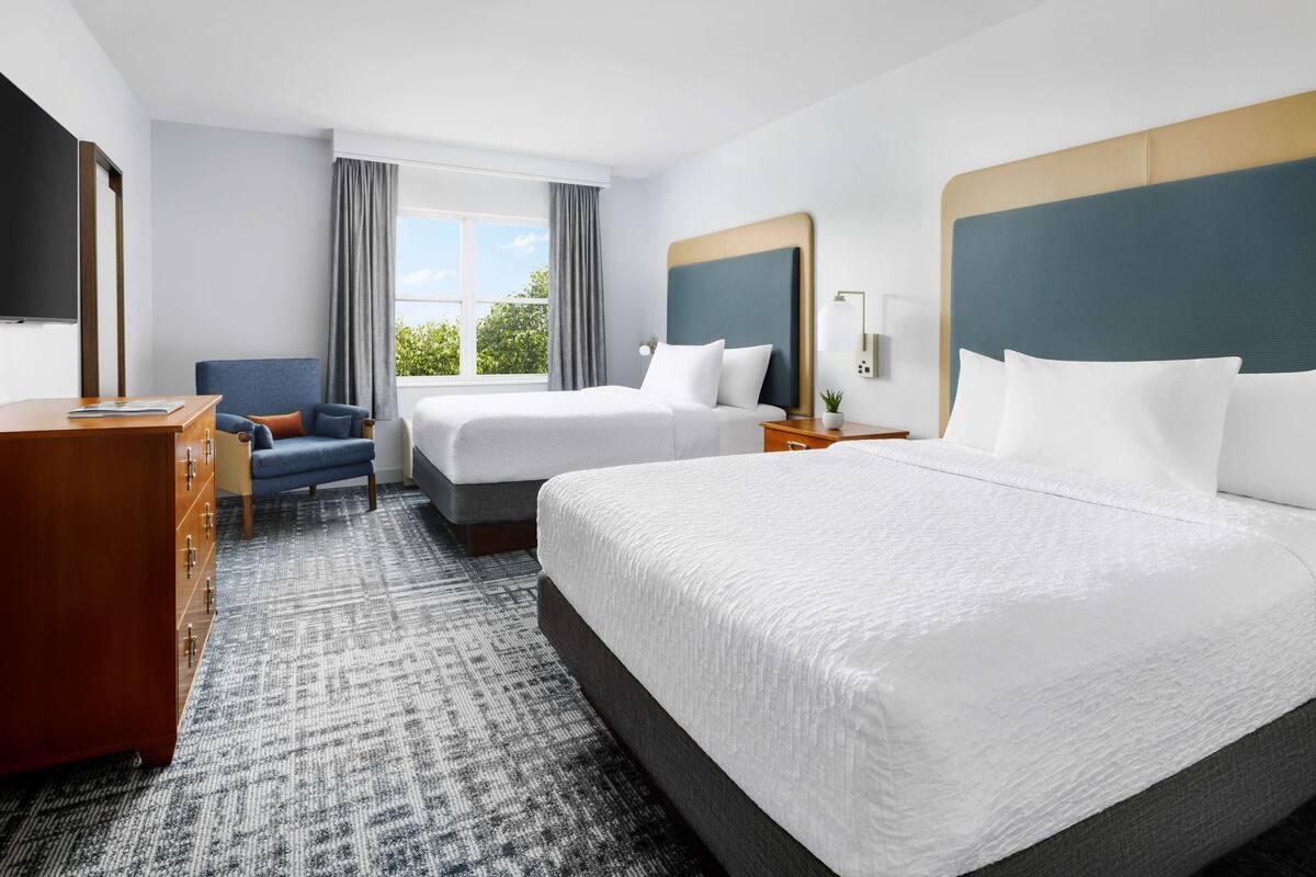 A hotel room with two beds, a desk, a dresser, and a TV.