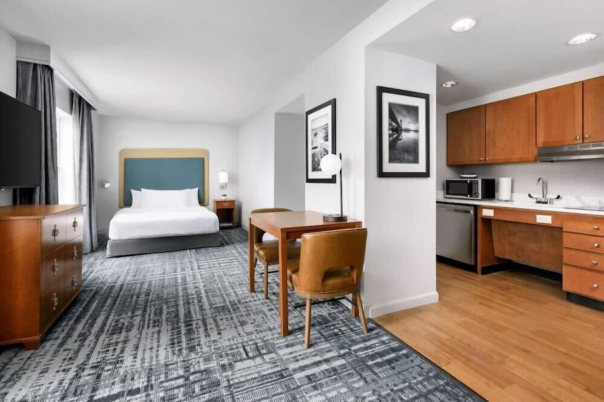A hotel room with a bed, a desk, a chair, a television, a microwave, and a kitchen area.