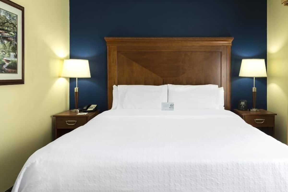A hotel room with a large bed, two bedside tables with lamps, a wooden headboard, and a framed picture on the wall.