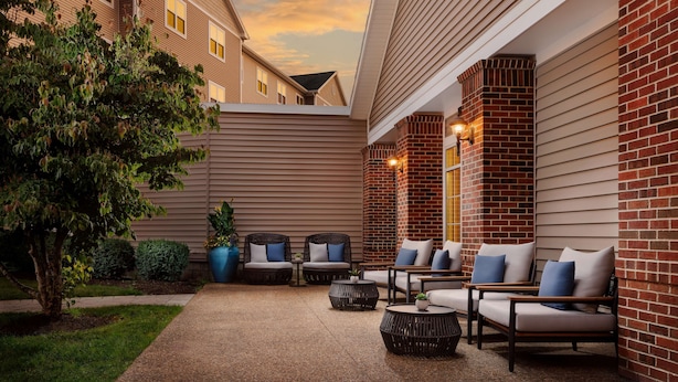 A courtyard with outdoor seating, a tree, and a brick wall. - Homewood Suites by Hilton Portsmouth (Portsmouth)