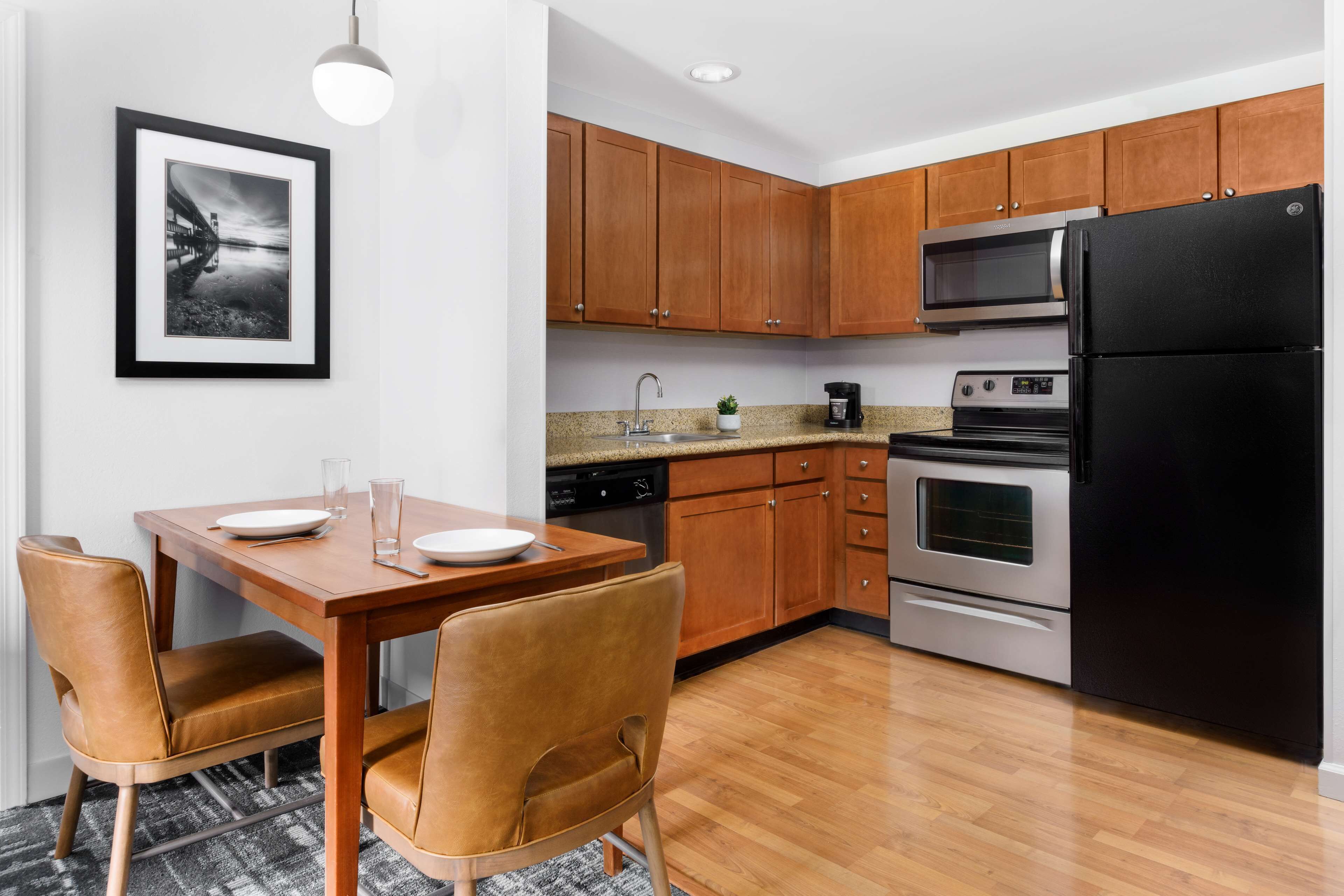 A modern kitchen with wooden cabinets, a black refrigerator, stainless steel appliances, and a dining area with a wooden table and leather chairs.