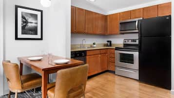 A modern kitchen with wooden cabinets, a black refrigerator, stainless steel appliances, and a dining area with a wooden table and leather chairs.