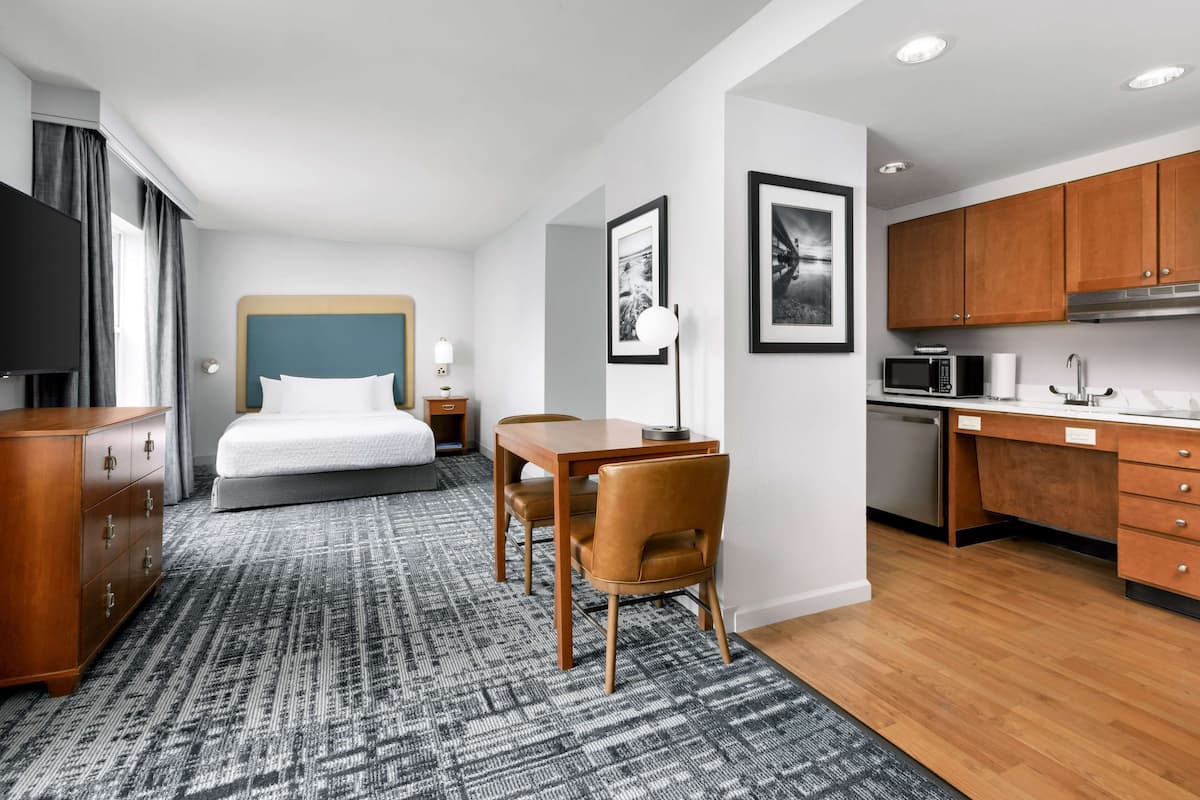 A hotel room with a bed, a desk, a chair, a television, a microwave, and a sink.
