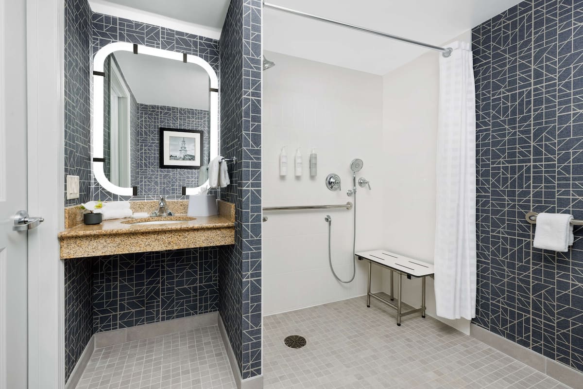 A modern bathroom with a granite countertop, a large mirror, a shower with a handheld showerhead, and a toilet.
