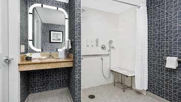 Een moderne badkamer met een granieten aanrecht, een grote spiegel, een douche met een handdouche en een toilet.