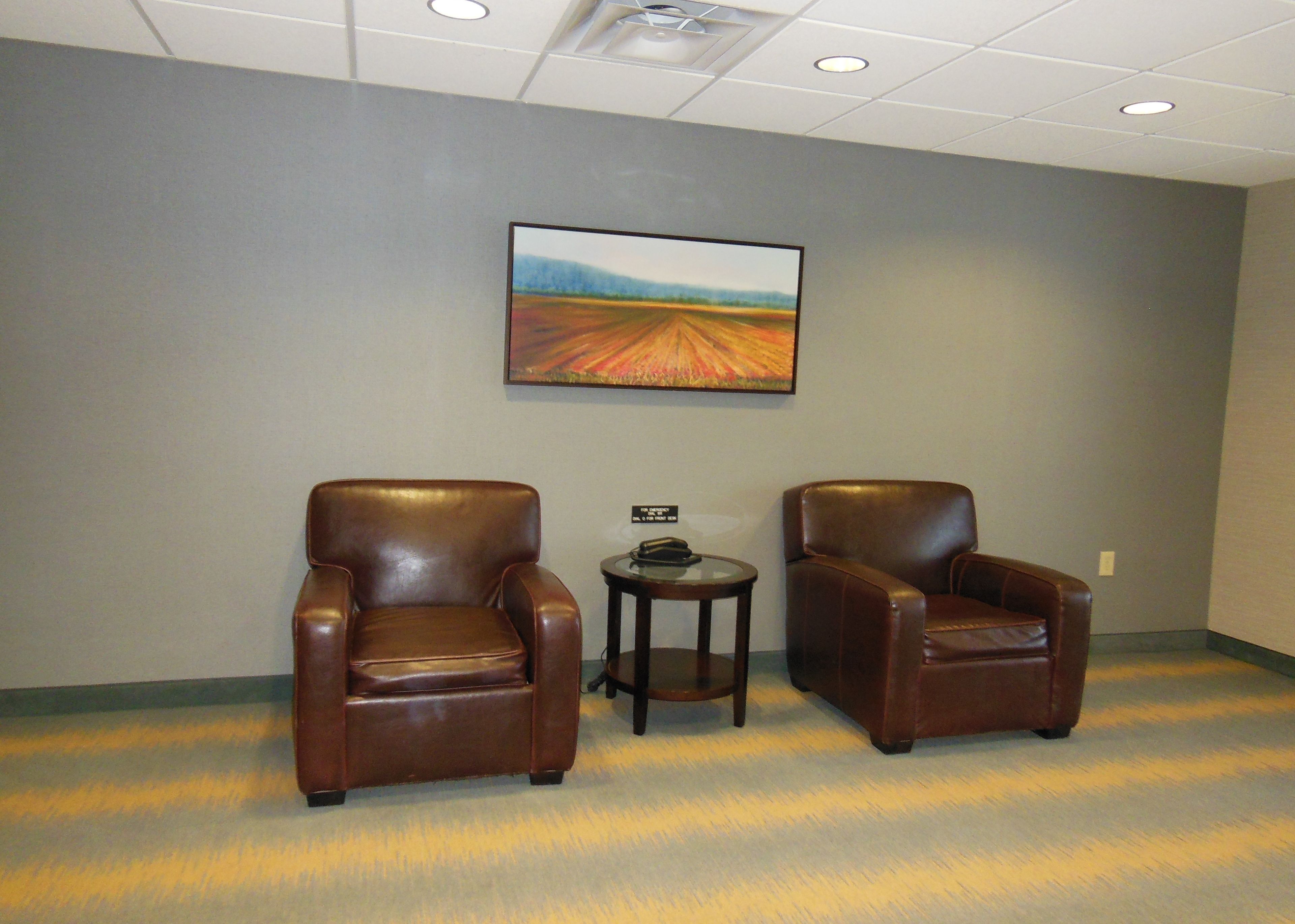 A room with two leather chairs, a small table, and a painting on the wall.