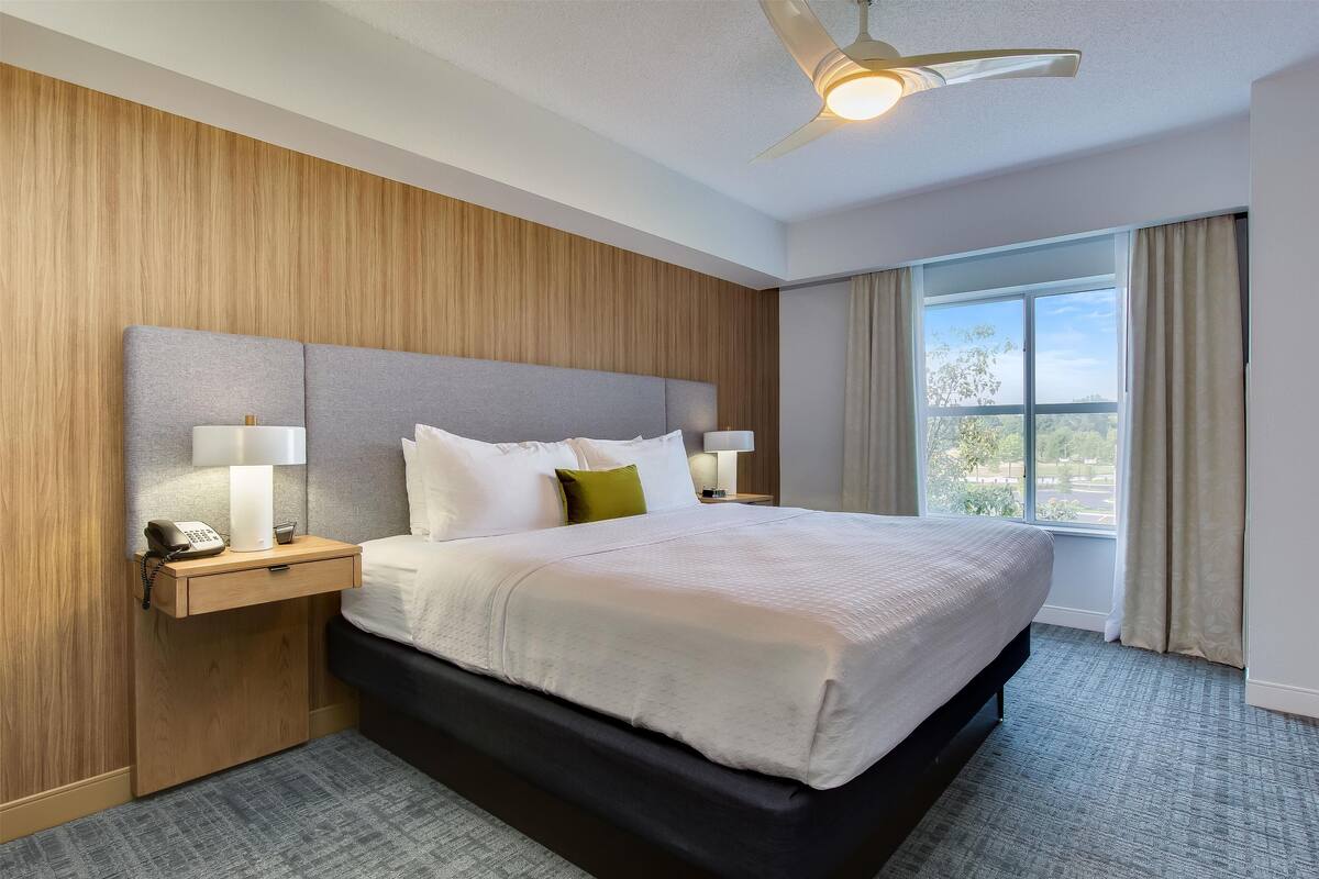 Una camera d'albergo con un letto grande, due comodini con lampade e una finestra con tende, oltre a una ventola a soffitto.