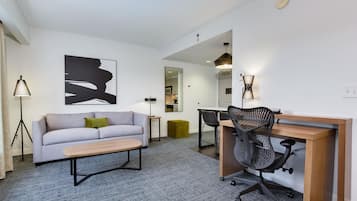 A modern living room with a sofa, a coffee table, a desk with a chair, a lamp, and a large abstract painting on the wall.
