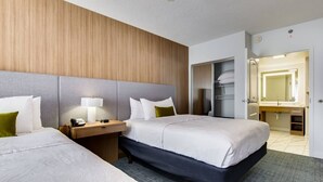 A hotel room with two beds, a bedside table with a lamp, a wardrobe, and a bathroom with a mirror and sink. - Homewood Suites by Hilton Louisville-East (Louisville)