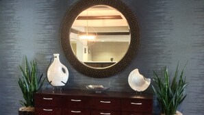 A reception area with a dark wood cabinet, a round mirror, and two potted plants. - Homewood Suites by Hilton Louisville-East (Louisville)