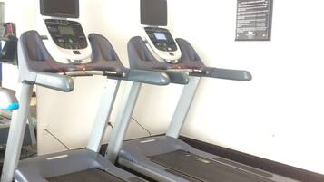 Three treadmills in a gym with a white wall and a sign about fitness center guidelines.