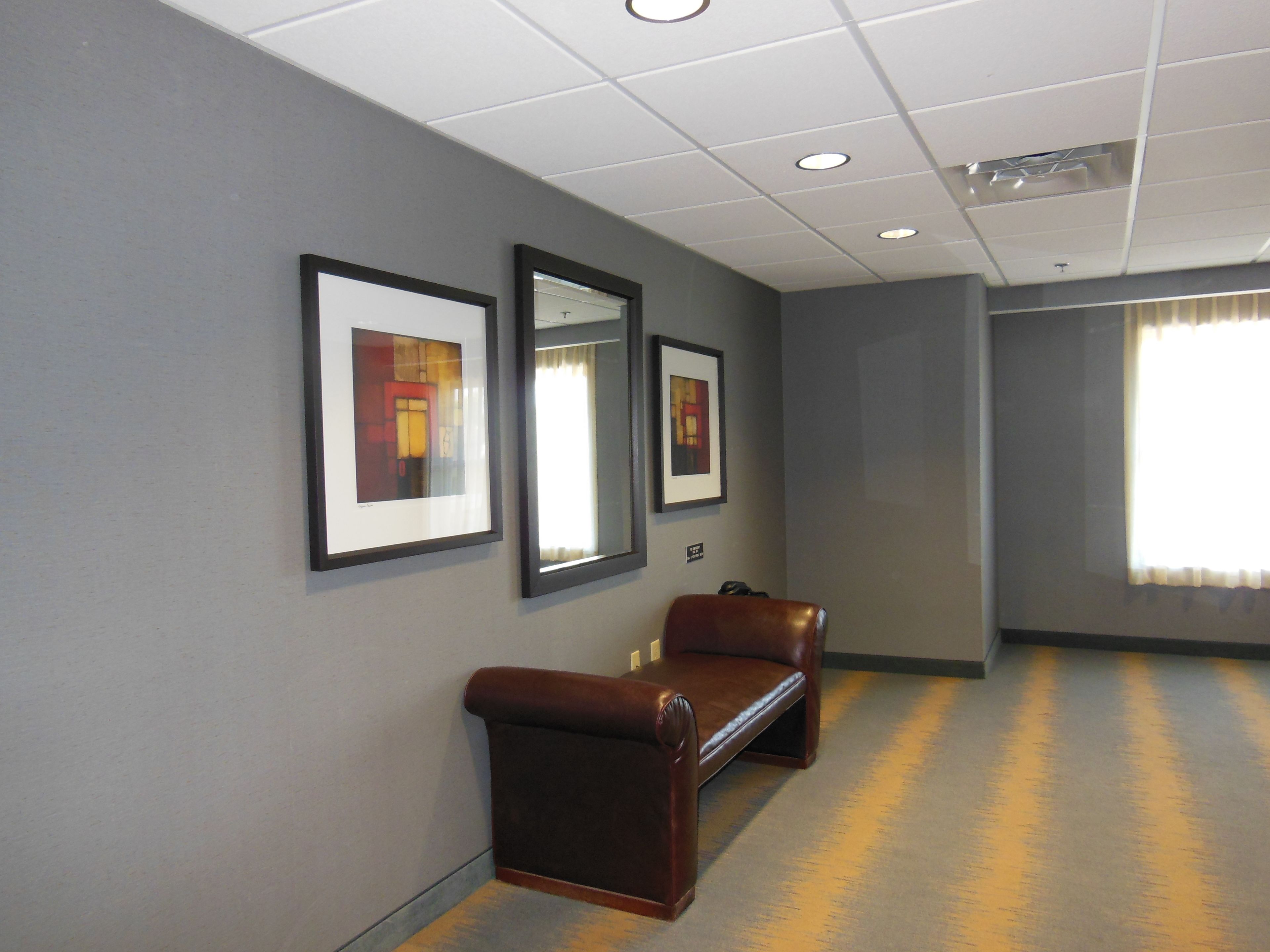 A hallway with framed artwork on the walls, a brown leather bench, and a carpeted floor.