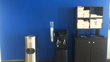 A blue wall, a trash can, a water dispenser, and a cabinet with folded towels.