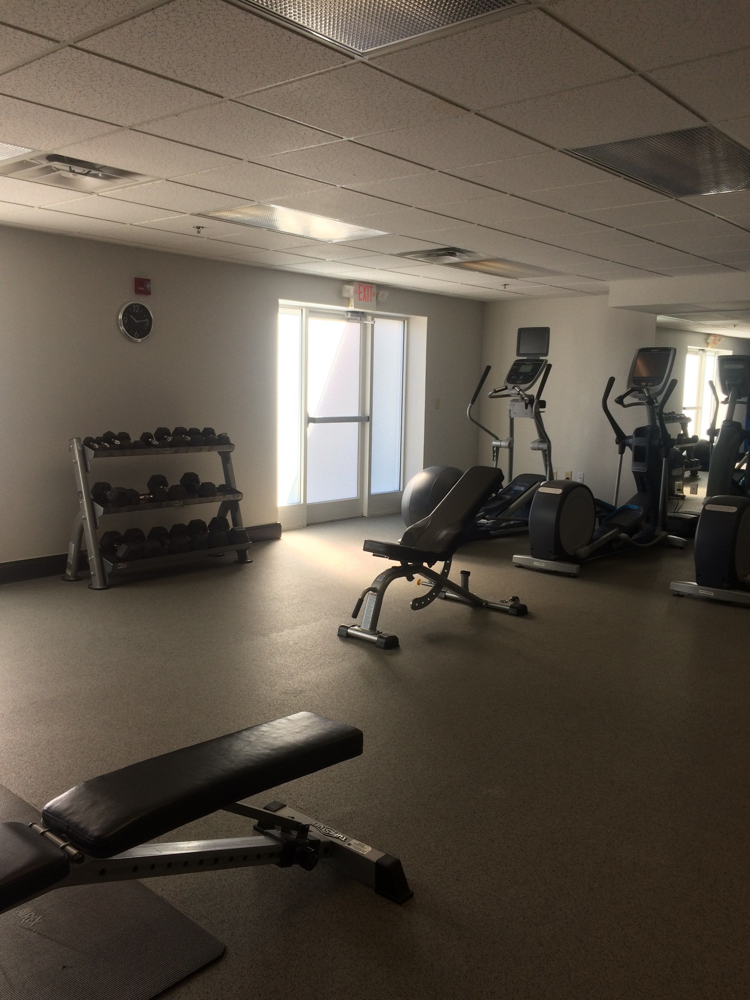 A gym with exercise equipment, a dumbbell rack, and a clock on the wall.