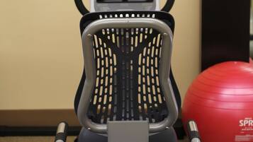 An exercise machine with a digital display and control panel, a black chair, and a red exercise ball.