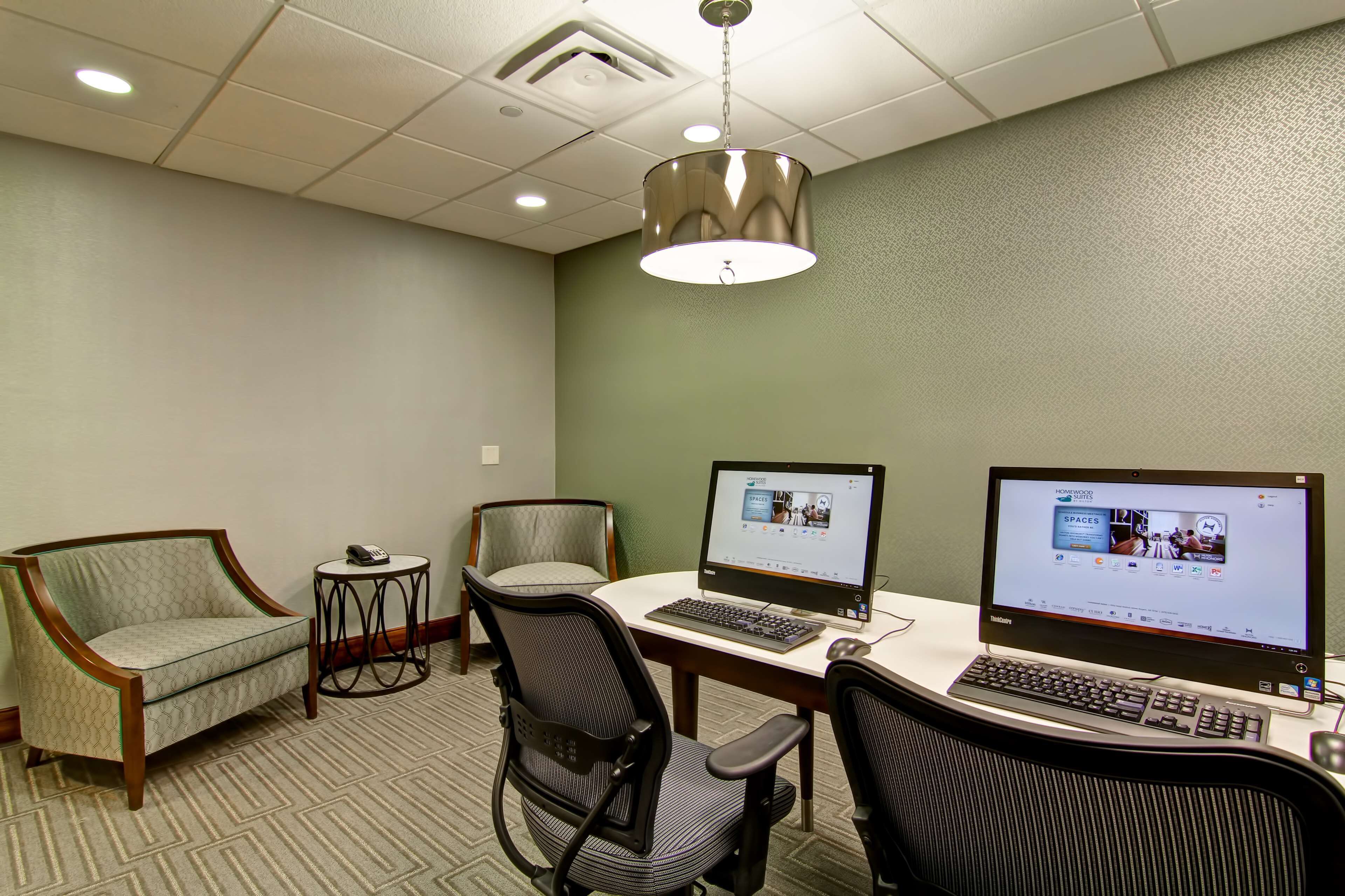 A hotel room with two computers, a desk, two chairs, and a small table.