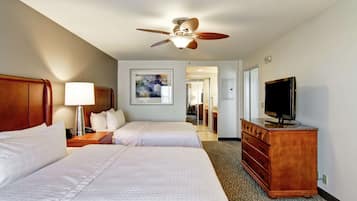 Habitación de hotel con dos camas, ventilador de techo, televisor y cómoda.