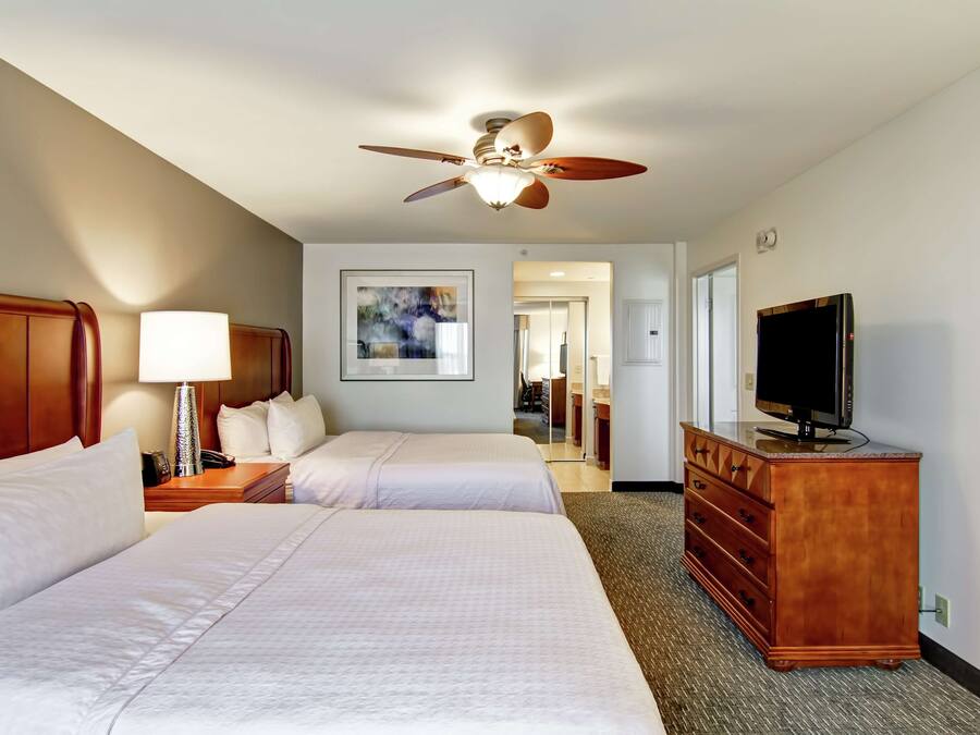 Habitación de hotel con dos camas, ventilador de techo, televisor y cómoda.