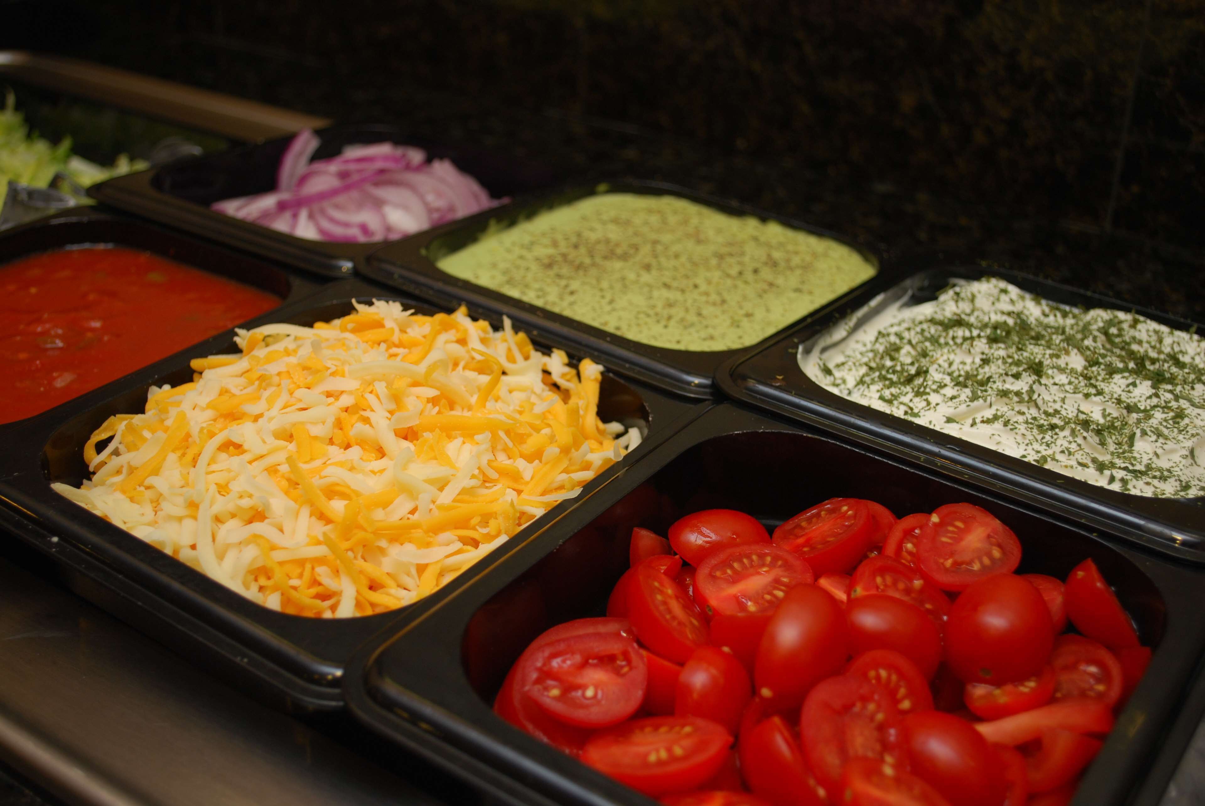 A buffet with various food items including shredded cheese, sliced tomatoes, and different sauces.
