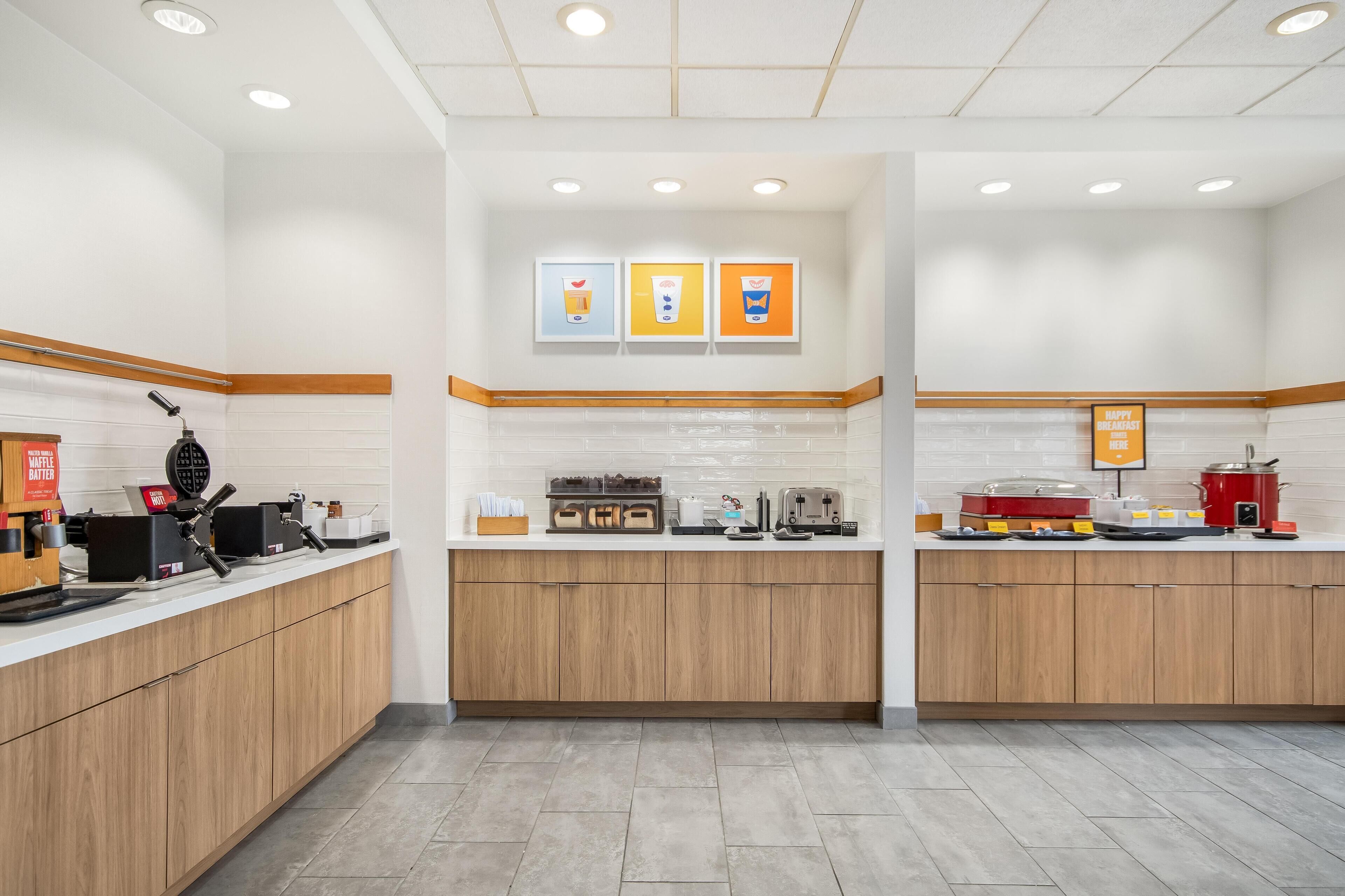A modern kitchen area with wooden cabinets, a coffee station, and a waffle maker.