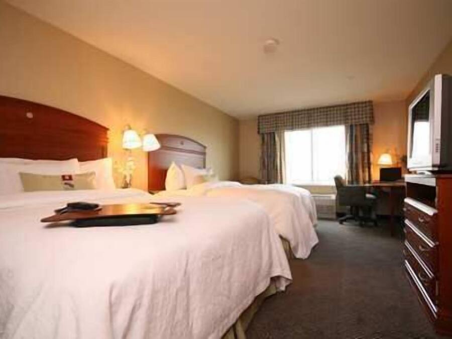 A hotel room with two beds, a desk, a chair, and a television.