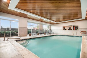 An indoor swimming pool with a wooden ceiling, large windows, and lounge chairs.