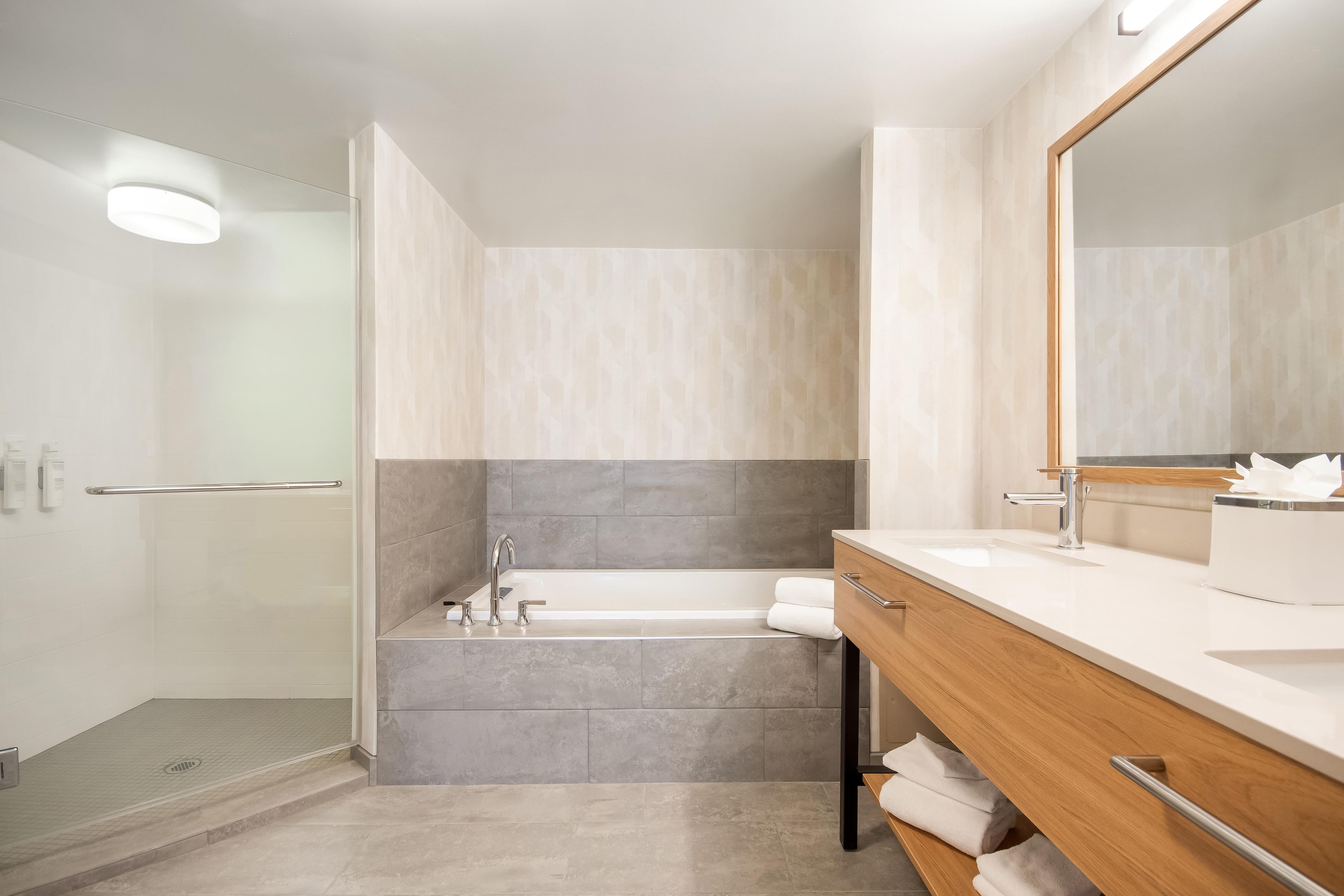 A modern bathroom with a bathtub, a vanity with a mirror, and a shower area.