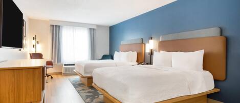 A hotel room with two beds, a desk, a flat-screen TV, and a large window with curtains.