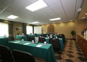 Un salón de conferencias con mesas, sillas y una pantalla de proyector.