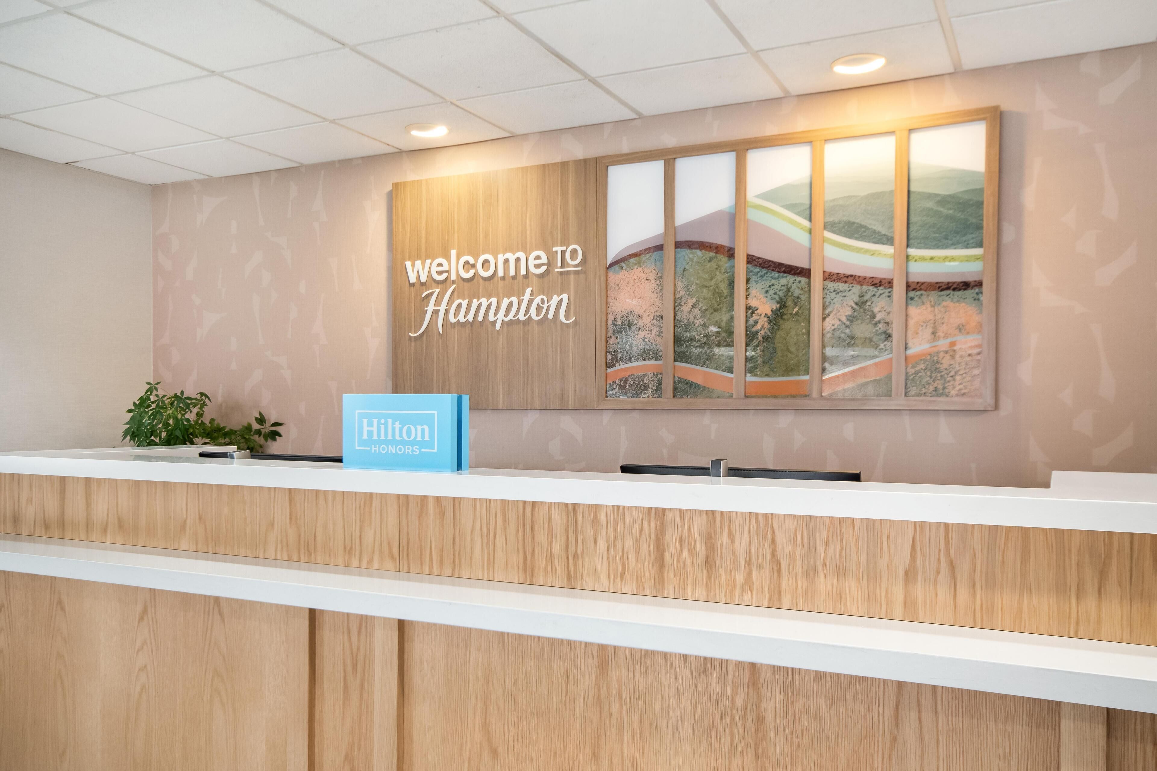 A reception desk with a 'Welcome to Hampton' sign and a 'Hilton Honors' sign.