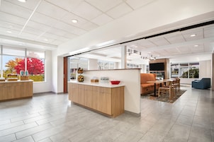A modern interior with a wooden reception desk, seating area, and large windows.