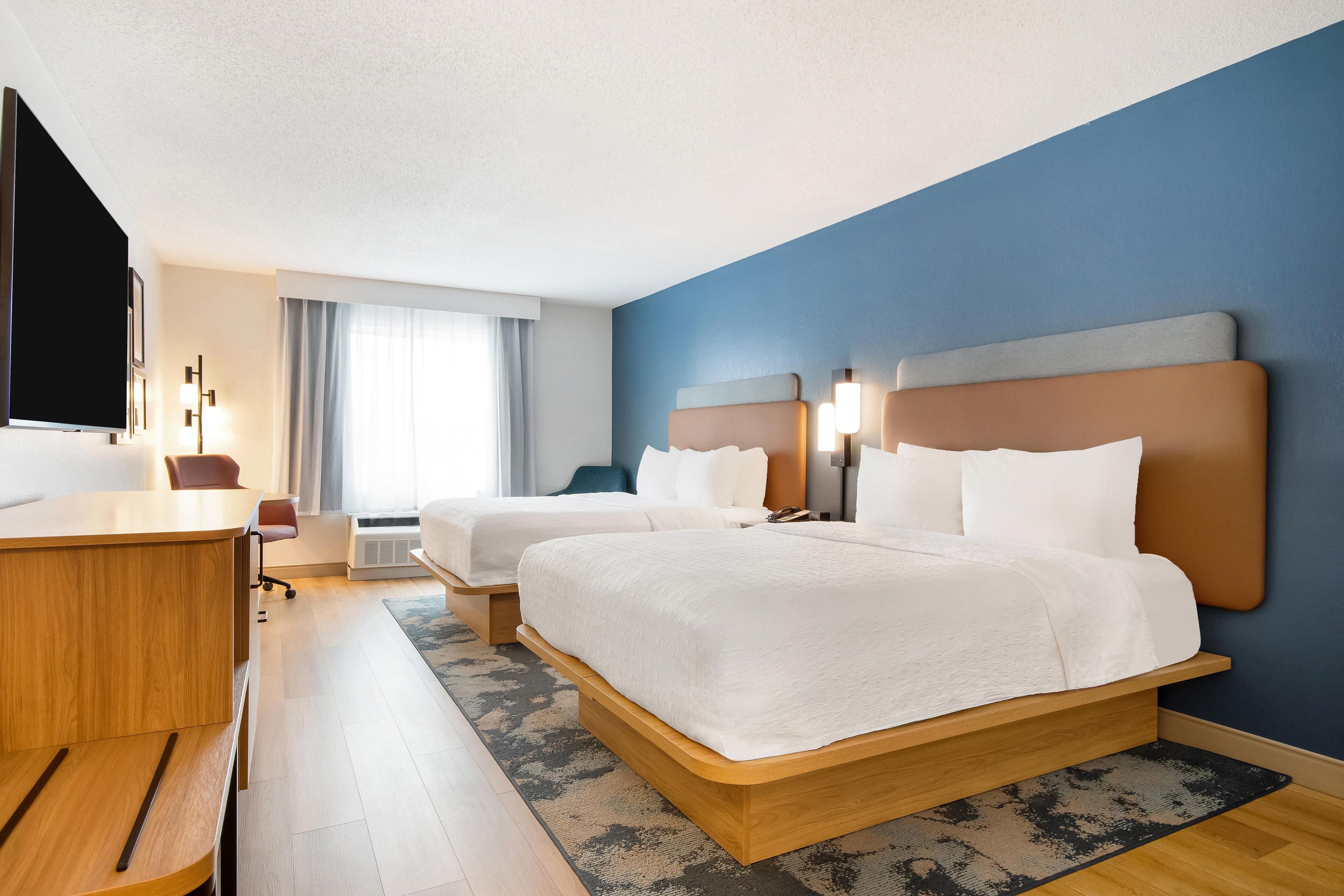 A hotel room with two beds, a desk, a chair, a television, and a window with curtains.