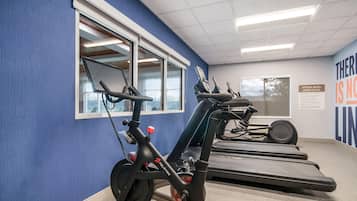 Uma sala de ginástica com equipamentos de exercício, incluindo bicicletas ergométricas e esteiras, e uma parede com texto motivacional.