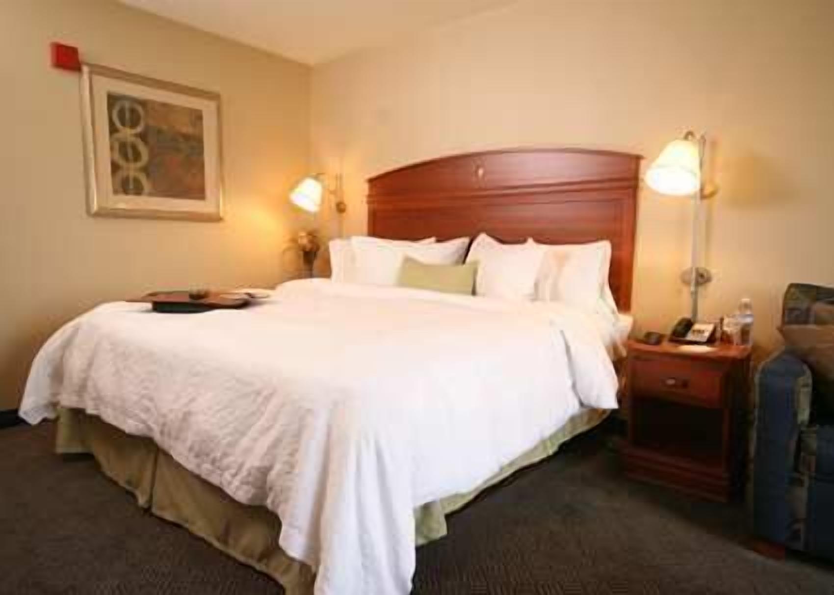 A hotel room with a large bed, a wooden headboard, two bedside tables with lamps, and a framed picture on the wall.