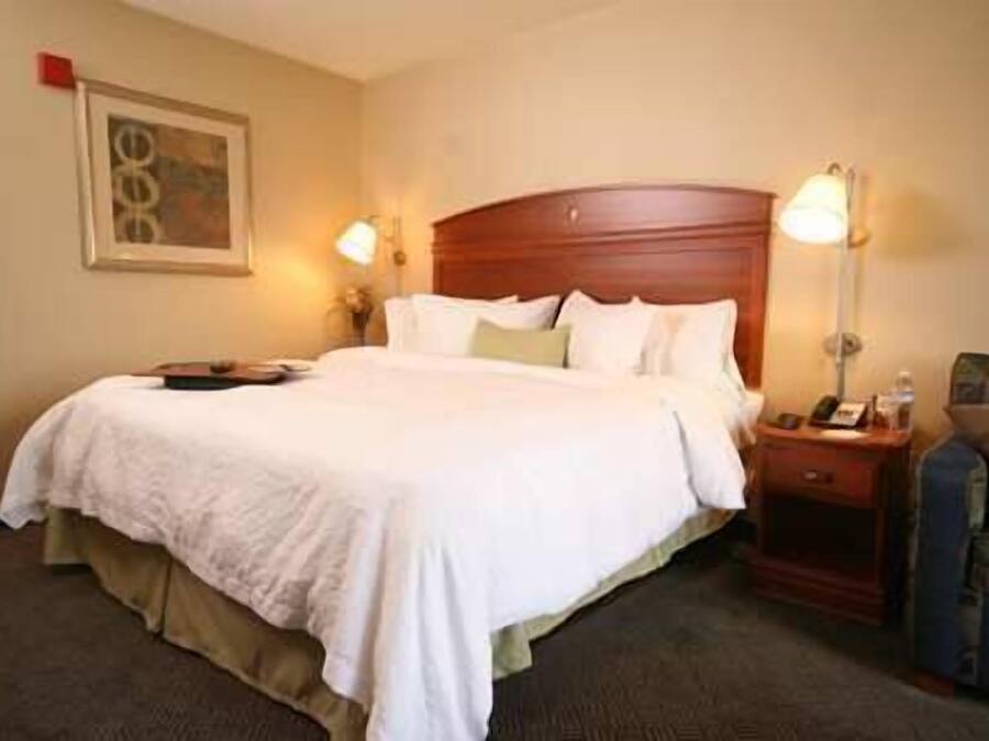 A hotel room with a large bed, a wooden headboard, two bedside tables with lamps, and a framed picture on the wall.