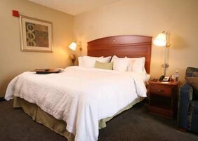 A hotel room with a large bed, a wooden headboard, two bedside tables with lamps, and a framed picture on the wall.