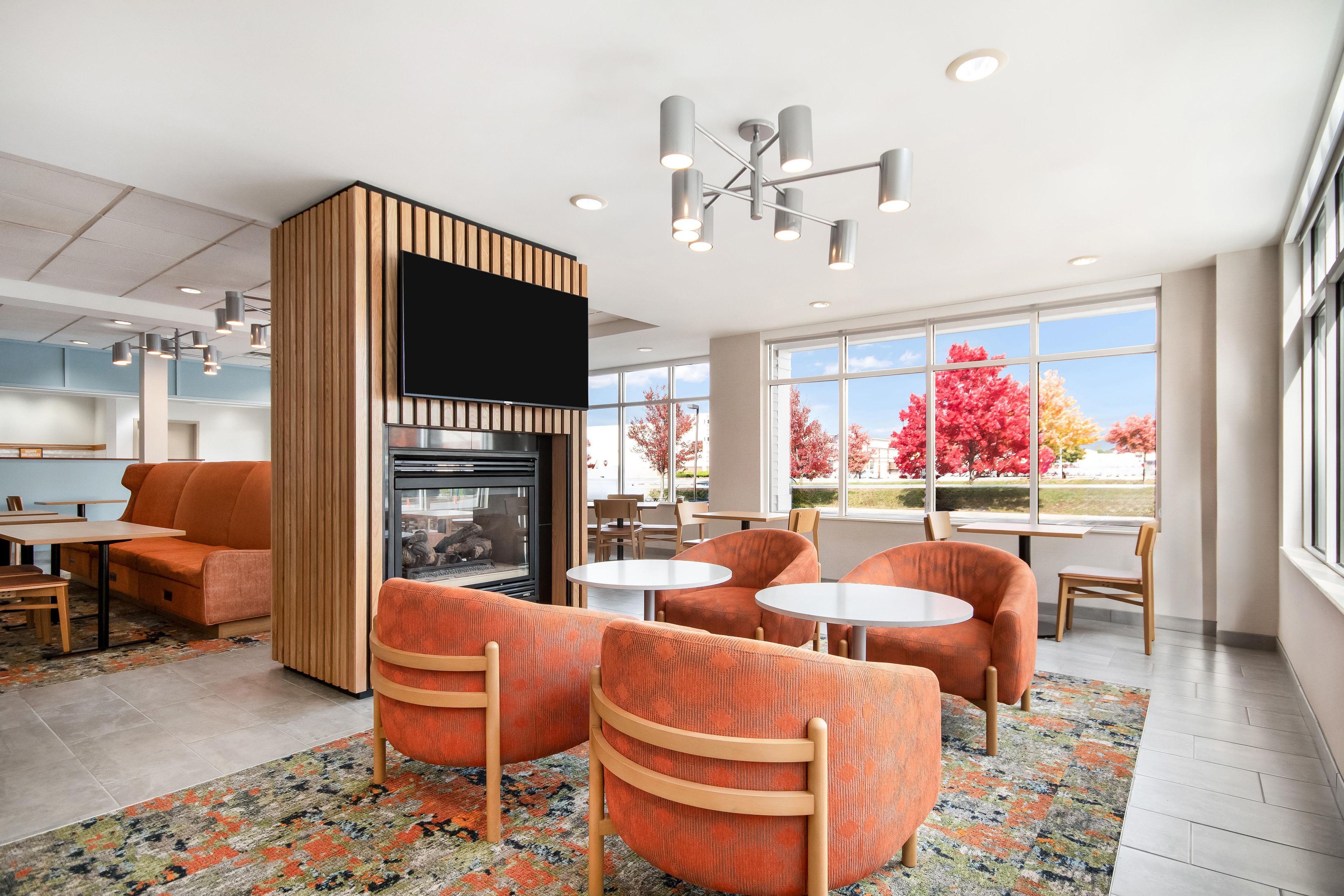 Un área de estar moderna con chimenea, asientos y grandes ventanales con vistas a árboles.