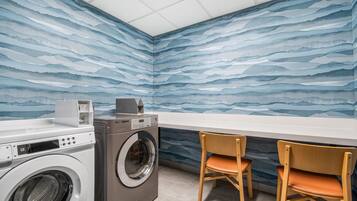 A laundry room with a washing machine, dryer, and two wooden chairs.