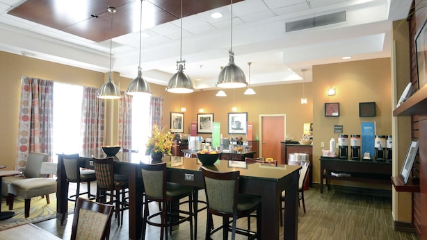A hotel dining area with a central island, multiple chairs, pendant lighting, and a coffee station. - Hampton Inn Vidalia (Vidalia)