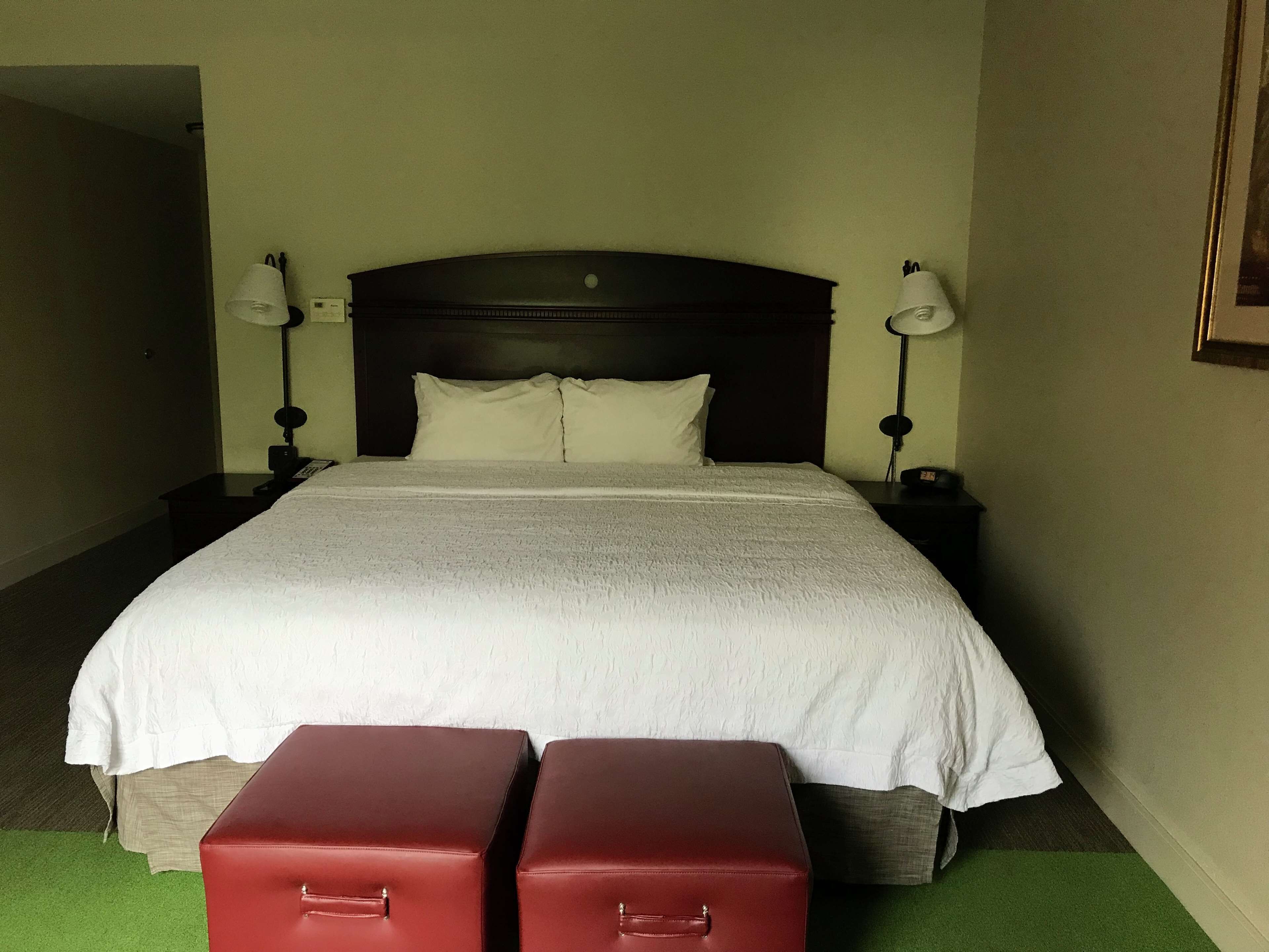 A hotel room with a large bed, two bedside lamps, a headboard, and two red suitcases.