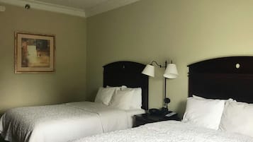 Habitación de hotel con dos camas individuales, una mesita de noche con lámpara, un cuadro en la pared y una pared de color claro.